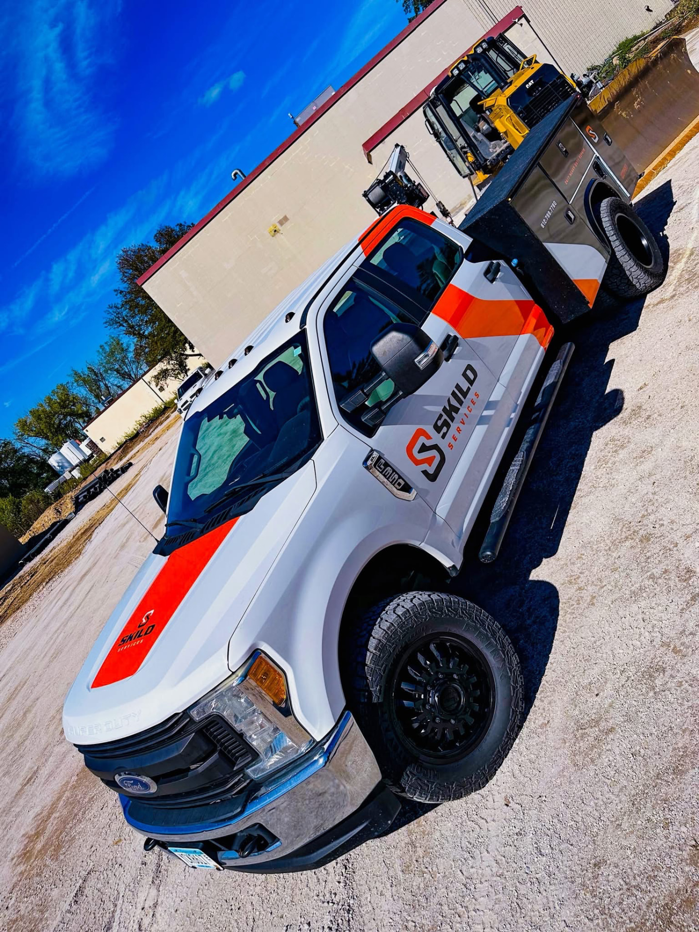 SKILD Services white Ford Super Duty mobile service truck with orange stripes hauling a CAT skid steer