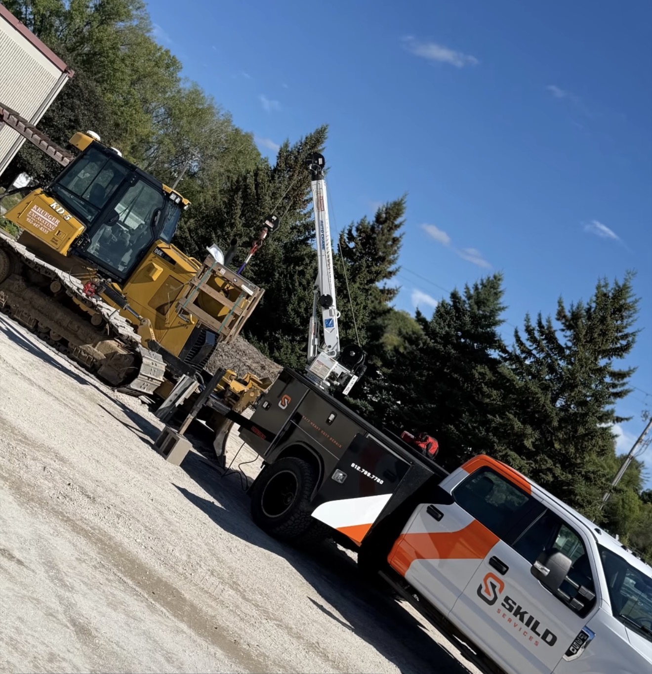 SKILD Services truck with a crane hoisting a component next to a tracked dozer on a gravel jobsite